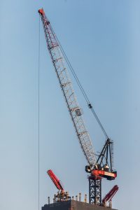 Crane modern sedang beroperasi di proyek konstruksi gedung tinggi dengan latar belakang langit biru
